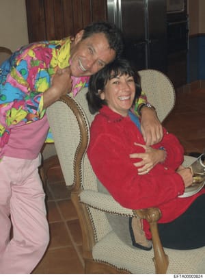 This is a casual photograph showing two people posing together indoors in what appears to be a residential setting. The image shows a man in colorful patterned clothing and a woman in red clothing, both smiling at the camera. The setting includes woo
