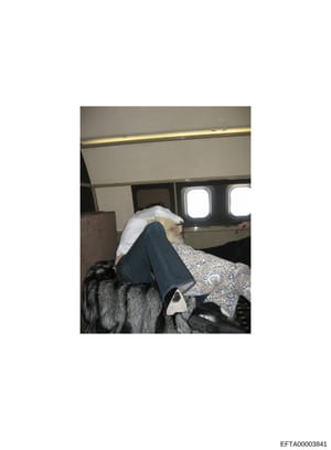 This is an evidence photograph showing the interior of what appears to be a private aircraft cabin. The image captures a person reclining on a seat with fur covering, wearing jeans and a patterned top with a white head covering. The photo documents t