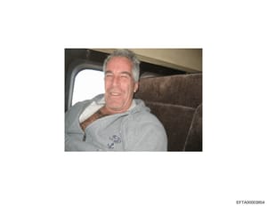 This is a candid photograph of Jeffrey Epstein seated inside what appears to be a private aircraft cabin. The image shows him wearing a gray hoodie with an anchor logo, seated on upholstered seating with an aircraft window visible in the background. 