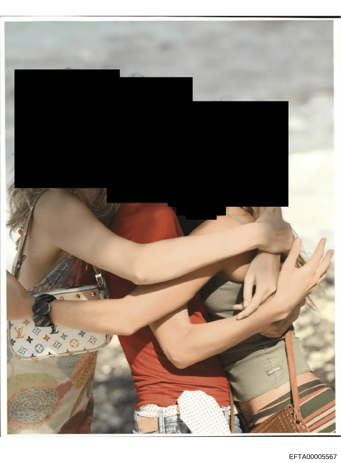This is a photograph showing two individuals at what appears to be a beach or outdoor waterfront location. The faces and upper portions of both individuals are heavily redacted with black boxes, obscuring their identities. The photo captures visible