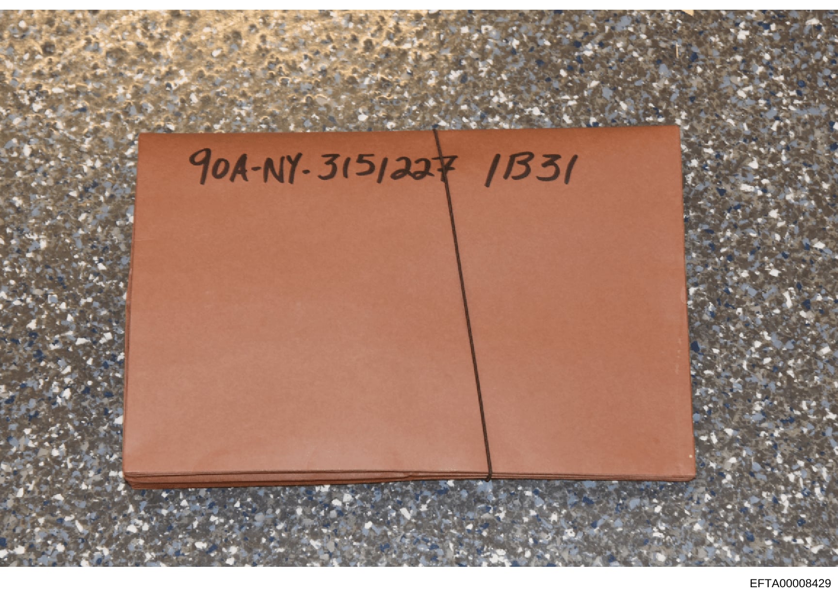 This is an evidence photograph showing a terra cotta/orange-colored envelope or folder placed on a granular surface. The envelope bears handwritten reference numbers '904-NY-315/227' and '1B31', which appear to be case or evidence identification code