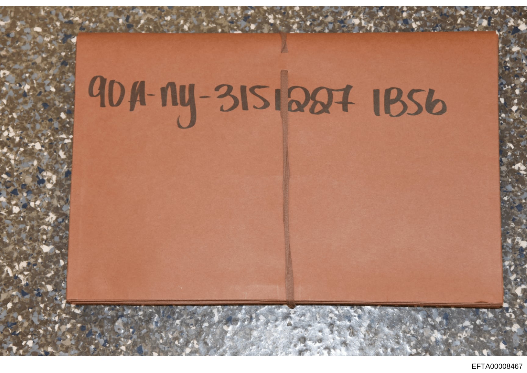 This is a photograph of a tan/orange evidence envelope or storage container with handwritten notations. The visible markings appear to be case reference numbers or file identifiers written in dark ink. The envelope is photographed lying flat on a tex