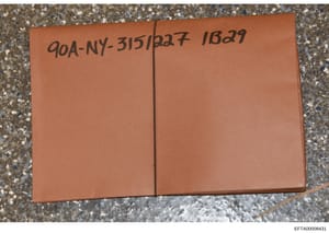 This is a photograph of a brown/tan sealed notebook or journal bearing handwritten case reference numbers (90A-NY-315/227 and 1B29). The document appears to be physical evidence collected during the investigation, photographed in place on a concrete 
