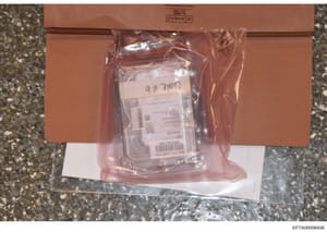This is an evidence photograph showing a sealed brown cardboard box containing a plastic bag with what appears to be a computer hard drive inside. The hard drive is labeled 'Comp # 6' and has an evidence label visible. The photograph documents the ph