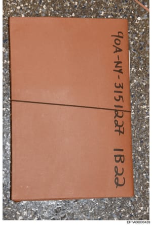 This is a photograph of a tan/terracotta colored leather-bound object, possibly a book, journal, or folder, photographed on a concrete surface. Handwritten text on the spine reads 'DOA-NY-315 Red 18 page'. The object appears to be physical evidence d
