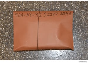 This is an evidence photograph showing a brown sealed envelope placed on a concrete surface. The envelope is marked with what appears to be a case identifier '904-NY-3' and numbers '57227 2B43', suggesting this is a physical evidence item catalogued 