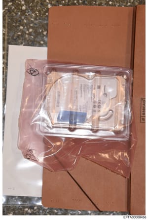 This photograph shows a computer hard drive sealed in anti-static pink packaging material placed on top of a brown cardboard box. The drive appears to be a Seagate or similar manufacturer based on visible labeling. This type of evidence photo documen