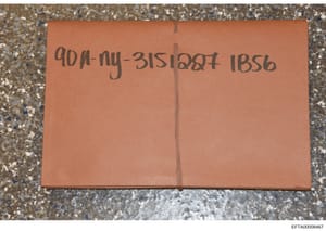 This is a photograph of a tan/orange evidence envelope or storage container with handwritten notations. The visible markings appear to be case reference numbers or file identifiers written in dark ink. The envelope is photographed lying flat on a tex